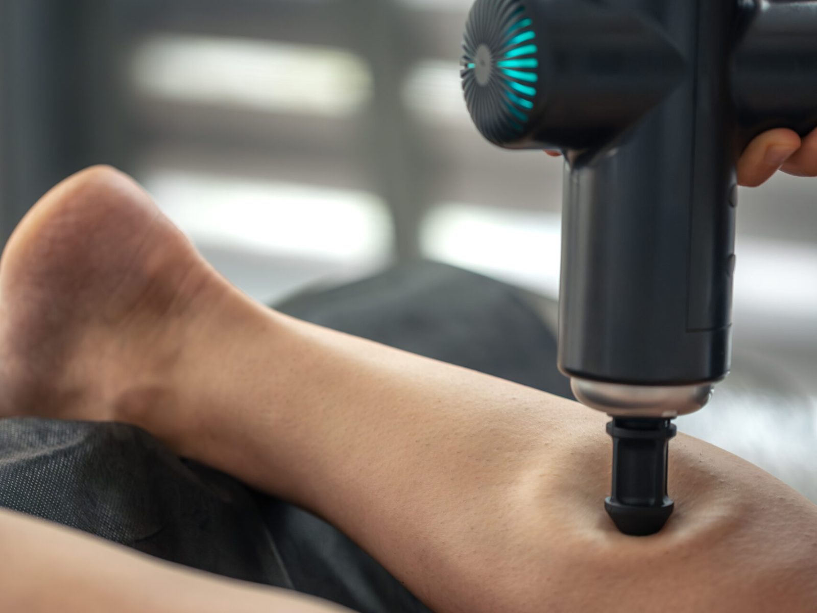 Gros plan d'un pistolet à percussion à tête conique travaillant le mollet. Pression ciblée pour la relaxation et la mobilité dans un contexte moderne de soins quotidiens.